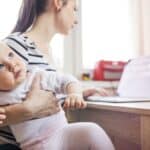 working mother on maternity leave using a laptop at home while caring for her baby