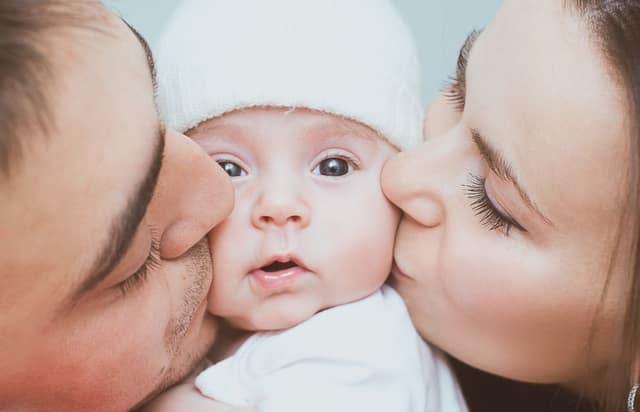 new parents kissing their newborn baby on the cheeks