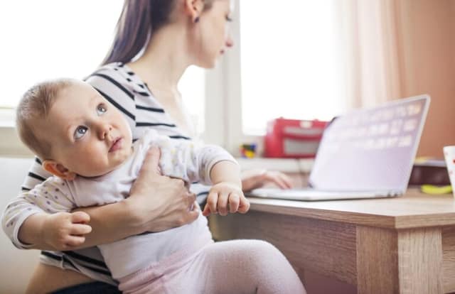 working mother on maternity leave using a laptop at home while caring for her baby