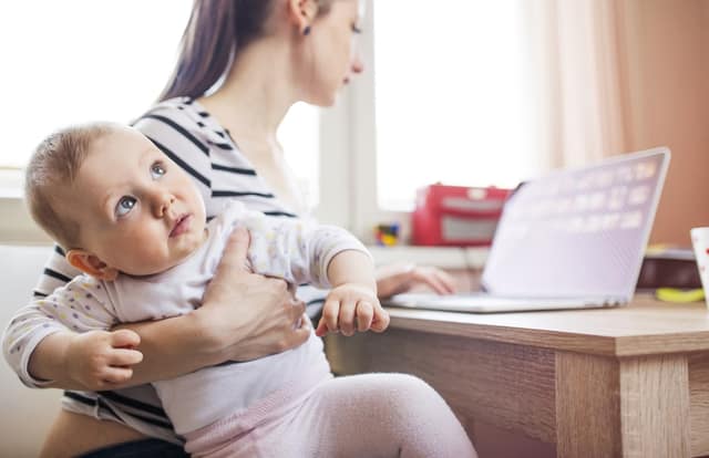 working mother on maternity leave using a laptop at home while caring for her baby