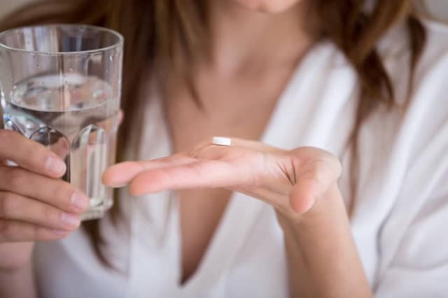 Morning after pill fertility woman holding emergency contraception pill with glass of water