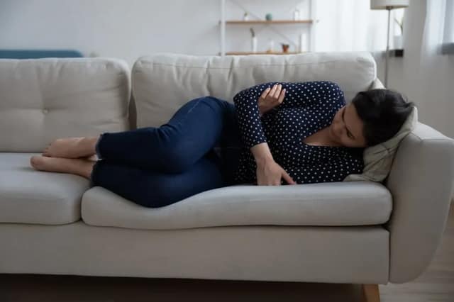 woman lying on a sofa holding her abdomen, representing miscarriage causes