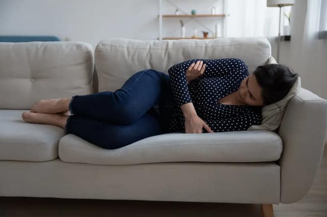 woman lying on a sofa holding her abdomen, representing miscarriage causes
