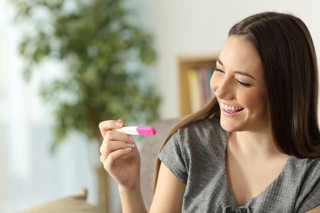 happy woman checking pregnancy test sitting