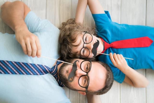 Non biological father: man and child playing with fake mustaches lying on the floor