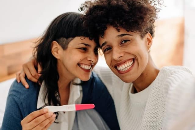 trying for a baby – same-sex female couple taking a selfie while holding a positive pregnancy test