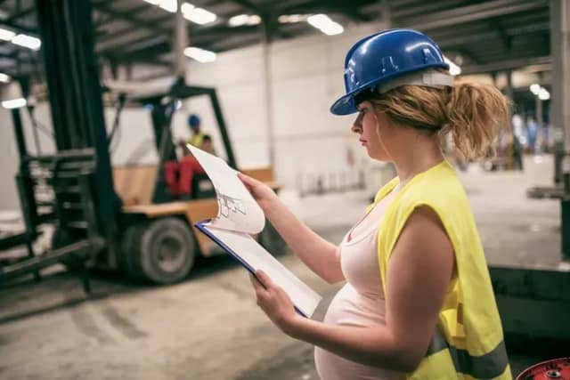 pregnancy discrimination showing pregnant woman at work reviewing documents in industrial workplace