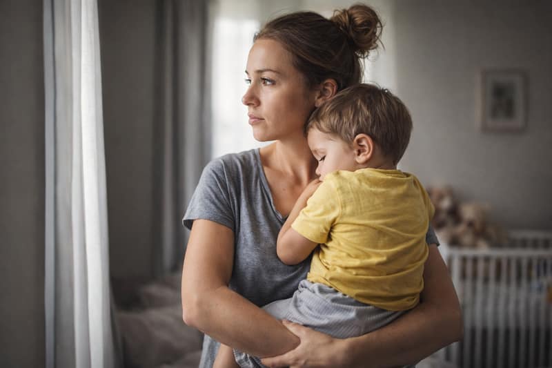 Becoming a single parent mother holding her child at home looking thoughtful