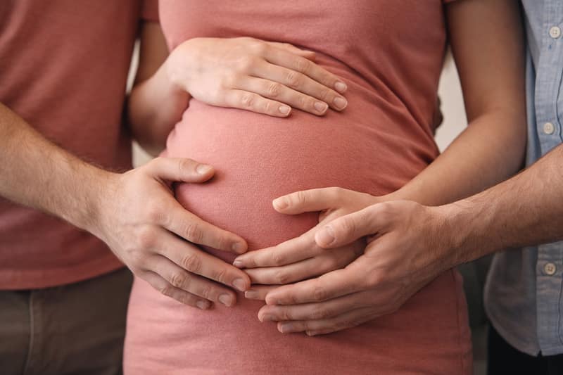 Surrogate pregnancy with intended parents placing hands on pregnant belly