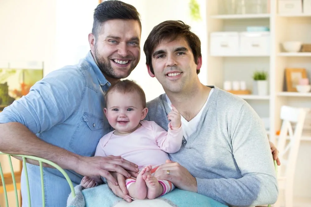 LGBT parenting – two fathers smiling with their baby at home in a loving family moment