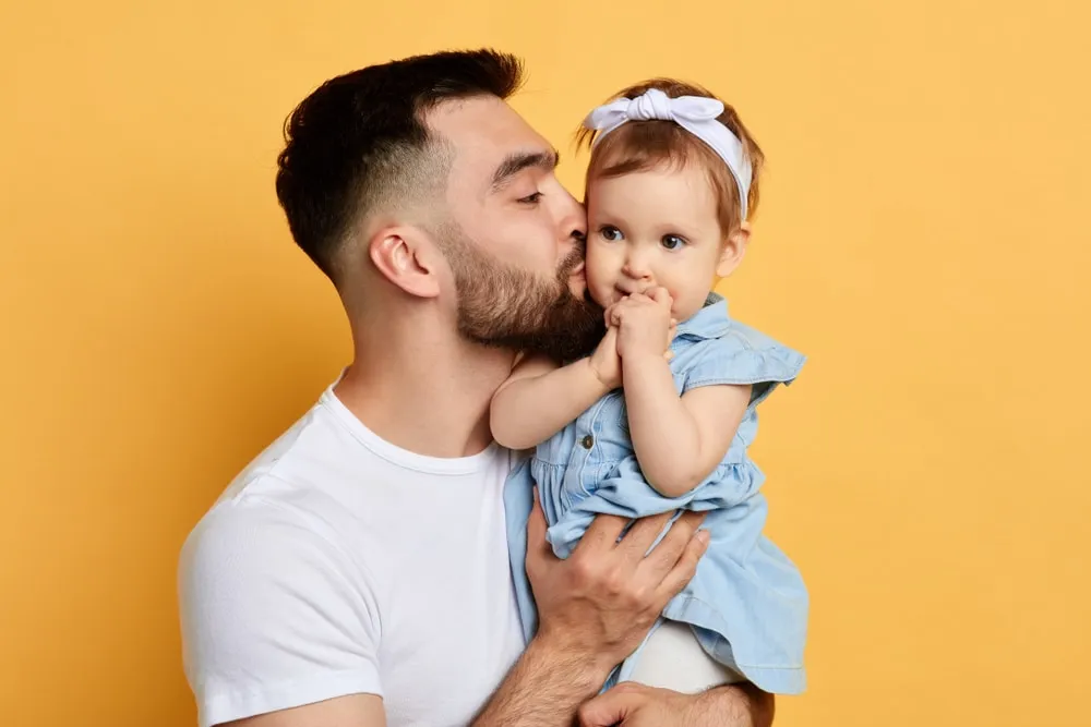 co parenting – father kissing his baby daughter while holding her in his arms